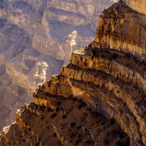 Sunlight illuminates the layered rock strata of a massive canyon wall, with deep shadows in the background.