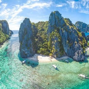 Vista aerea di isole rocciose e ricoperte di vegetazione, con barche a bilanciere su acque limpide e turchesi, vicino a una piccola spiaggia sabbiosa.