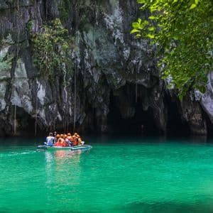 Un viaggio di gruppo WeRoad in barca a remi su acque turchesi verso l'ingresso di una grande grotta in una scogliera rocciosa.