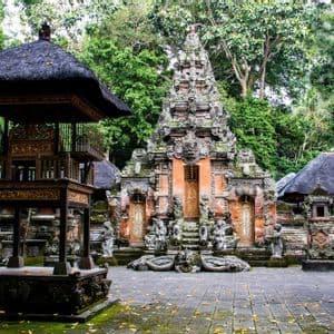 Un tempio ornato con sculture in pietra e tetti di paglia si erge in un cortile circondato da una foresta lussureggiante.