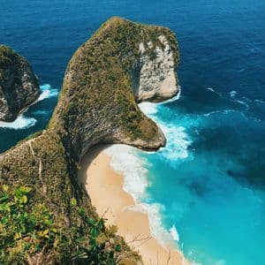 Una vista dall'alto di un'ampia scogliera ricoperta di verde che si estende su una spiaggia appartata con acqua turchese.