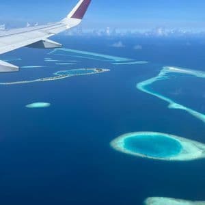 Una vista aerea dal finestrino di un aereo mostra la sua ala su un oceano blu profondo con atolli tropicali e banchi di sabbia.
