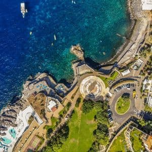 Una vista aerea, dall'alto, di un resort costiero con piscine e parchi verdi che costeggiano un oceano blu intenso.