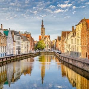 Un canal central reflète des bâtiments historiques à pignons et un haut clocher sous un ciel partiellement nuageux.