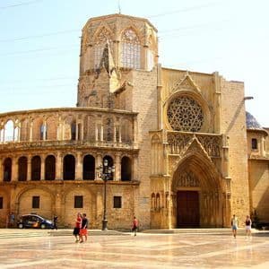 La facciata di una grande cattedrale gotica con rosone, vista da un'ampia piazza assolata.