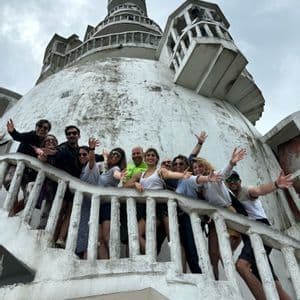 Un gruppo WeRoad in viaggio posa e saluta dalla scalinata di un ampio edificio bianco con cupola, sotto un cielo nuvoloso.