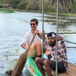 Zwei Männer einer WeRoad Gruppenreise in einem grünen Kanu auf einem See, einer paddelnd und der andere auf der Plattform sitzend.