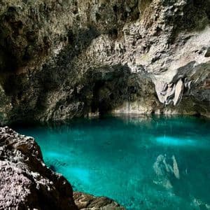 Una piscina di acqua limpida e turchese all'interno di una grotta rocciosa con stalattiti che pendono dal soffitto.