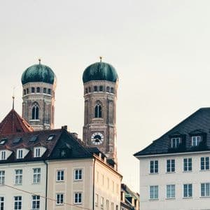 Le torri gemelle di una cattedrale con cupole verdi e un orologio si ergono sopra i tetti degli edifici della città contro un cielo pallido.