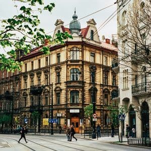 Un edificio de esquina ornamentado en una calle de la ciudad con vías de tranvía y peatones cruzando en una intersección.