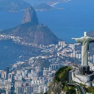 Una gran estatua con brazos extendidos en la cima de una montaña, dominando una extensa ciudad costera y una gran bahía con otra montaña.