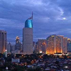 Uno skyline cittadino esteso con grattacieli illuminati al tramonto sotto un cielo nuvoloso e blu scuro.