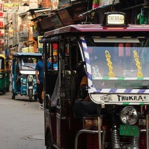 Una fila di coloratissimi risciò a motore, o tuk-tuk, su una trafficata strada cittadina, affollata di pedoni e insegne.