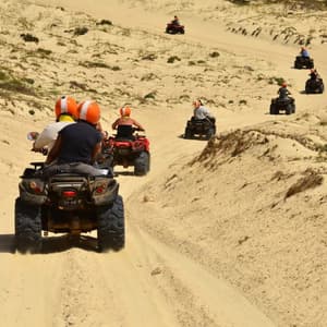 Un viaggio di gruppo WeRoad in quad, in fila su una pista sabbiosa tra dune ondulate.
