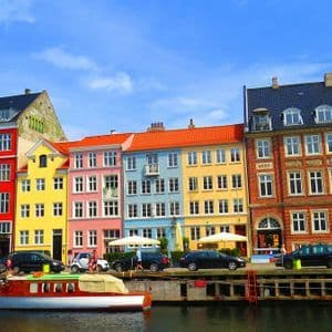 Eine Reihe bunter Gebäude säumt einen Kanal, auf dem Boote liegen und entlang der Straße Autos parken.