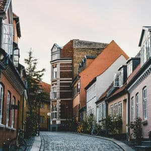 Eine geschwungene Kopfsteinpflasterstraße wird von bunten historischen Gebäuden gesäumt, daneben stehen mehrere Fahrräder.