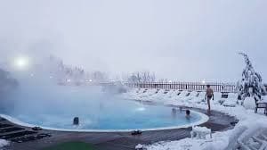 A few people relax in a steaming outdoor pool surrounded by a landscape completely covered in snow.
