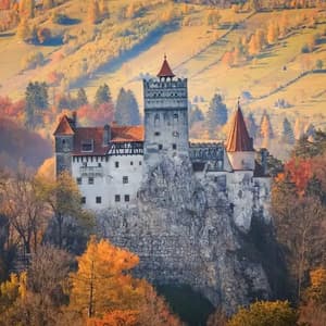 Un castillo medieval con tejados rojos se alza sobre un acantilado rocoso, rodeado por un bosque con follaje otoñal colorido.