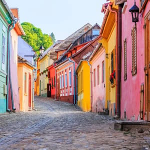Una estrecha calle empedrada y vacía serpentea cuesta arriba, flanqueada por edificios históricos de colores vivos bajo un cielo despejado.