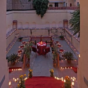 Una mesa de comedor para cuatro con un mantel rojo en un patio de piedra hundido, iluminada por docenas de velas.