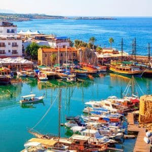 Vue aérienne d'un port animé, rempli de bateaux et de yachts amarrés dans des eaux turquoise, jouxtant une ville côtière sous un ciel dégagé.