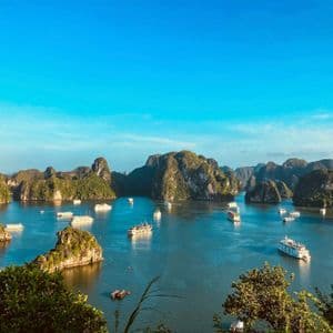 Una vista aerea di una baia gremita di numerose imbarcazioni che navigano tra grandi formazioni rocciose ricoperte di verde, sotto un cielo azzurro e limpido.