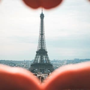 La Torre Eiffel incorniciata da un cuore formato dalle mani, con lo skyline della città sullo sfondo.