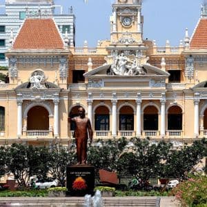 Una statua di bronzo di una figura politica si trova in un giardino di fronte all'ornato e giallo palazzo del Municipio di Ho Chi Minh.