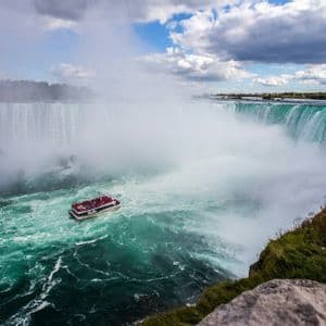 Una barca turistica con passeggeri naviga le acque turchesi, agitate e nebbiose, ai piedi di un'imponente cascata.
