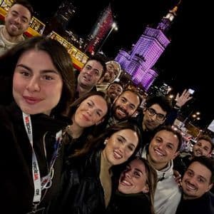 Un gruppo WeRoad scatta un selfie di notte in una città, con una torre illuminata e un tram sullo sfondo.