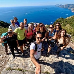 Un gruppo di escursionisti WeRoad si scatta un selfie su una scogliera soleggiata a picco sul mare blu e la costa.