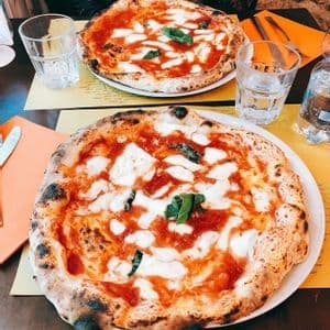Two Neapolitan pizzas topped with fresh mozzarella and basil resting on a restaurant table with glasses of water.