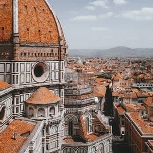 Le grand dôme aux tuiles rouges d'une cathédrale domine un paysage urbain de bâtiments aux toits rouges et des montagnes lointaines.