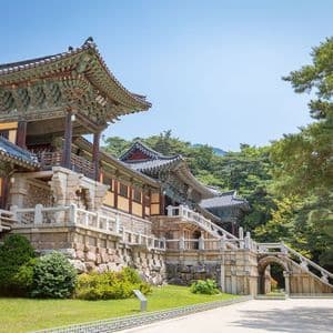 Un ornato e tradizionale complesso di templi dell'Asia orientale, edificato su fondamenta di pietra, con alberi rigogliosi e un cielo azzurro limpido sullo sfondo.