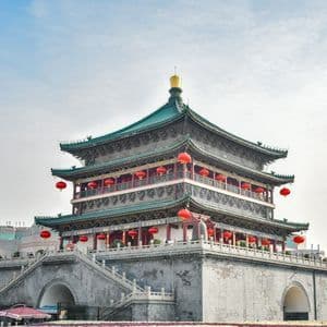Un tradizionale edificio cinese a più livelli, con tetti verdi e lanterne rosse, si erge contro lo skyline di una città sotto un cielo azzurro.