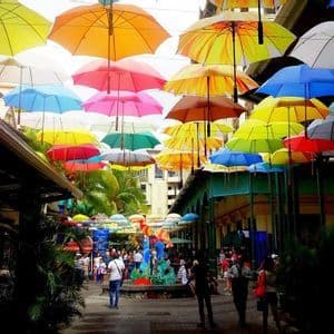 Un baldacchino di ombrelli multicolori pende su una vivace strada cittadina piena di pedoni e negozi.
