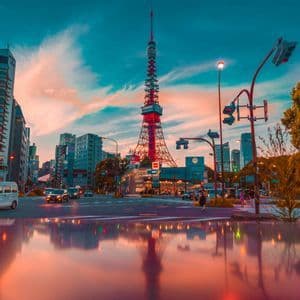 La Torre di Tokyo rossa si erge su un paesaggio urbano al tramonto, il suo riflesso visibile su una strada bagnata in primo piano.