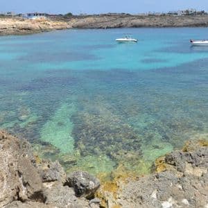 Due barche bianche ancorate in una baia tranquilla con acqua cristallina turchese e una costa rocciosa sullo sfondo.