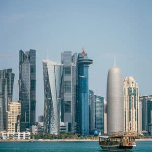 Una barca tradizionale in legno naviga su acque turchesi, con i moderni grattacieli di uno skyline cittadino sullo sfondo.