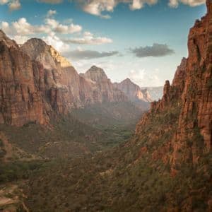 Un'ampia veduta di un canyon di roccia rossa con una rigogliosa valle verde sottostante, sotto un cielo azzurro parzialmente nuvoloso.