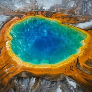 Una veduta aerea dall'alto di una sorgente geotermica con acqua blu vivace, circondata da anelli minerali arancioni e gialli brillanti.