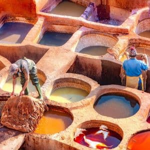 Dos trabajadores tiñen pieles de animales en grandes cubas de piedra llenas de líquidos coloridos en una curtiduría tradicional.