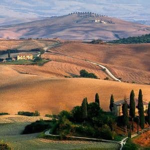 Una vista suggestiva di ville e cipressi sparsi su dolci colline dorate sotto un cielo velato.