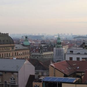 Vista aerea di una città europea con un grande edificio a cupola e guglie verdi sotto un cielo nebbioso e coperto.