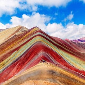Un grupo de WeRoad en la cima de una vibrante montaña multicolor, bajo un cielo azul con nubes.