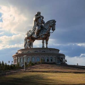 Una gigantesca statua equestre d'argento di un guerriero si erge su un edificio circolare su una collina erbosa sotto un cielo parzialmente nuvoloso.
