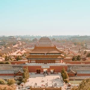 Una veduta dall'alto di un grande complesso palaziale asiatico tradizionale, caratterizzato da edifici rossi e tetti di tegole sotto un cielo sereno.