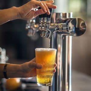 Primer plano de manos sirviendo una cerveza dorada de un grifo cromado brillante en un vaso de pinta.