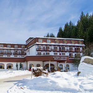 El edificio del Alpen Hotel Weitlanbrunn se alza en un paisaje nevado, con un denso bosque de pinos en la montaña detrás.
