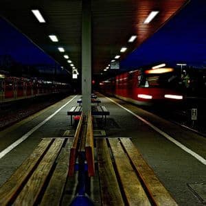 Un treno rosso sfreccia di notte davanti a una banchina della stazione vuota e illuminata, creando un effetto di mosso.